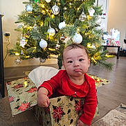 Thomas joined the competition — help win amazing prizes! baby, child, christmas_tree, gift_box, holiday, decorations, ornaments, lights, red_clothing, floor, indoor, home, cute, festive, smiling, person, celebration, seasonal, toddler, playful