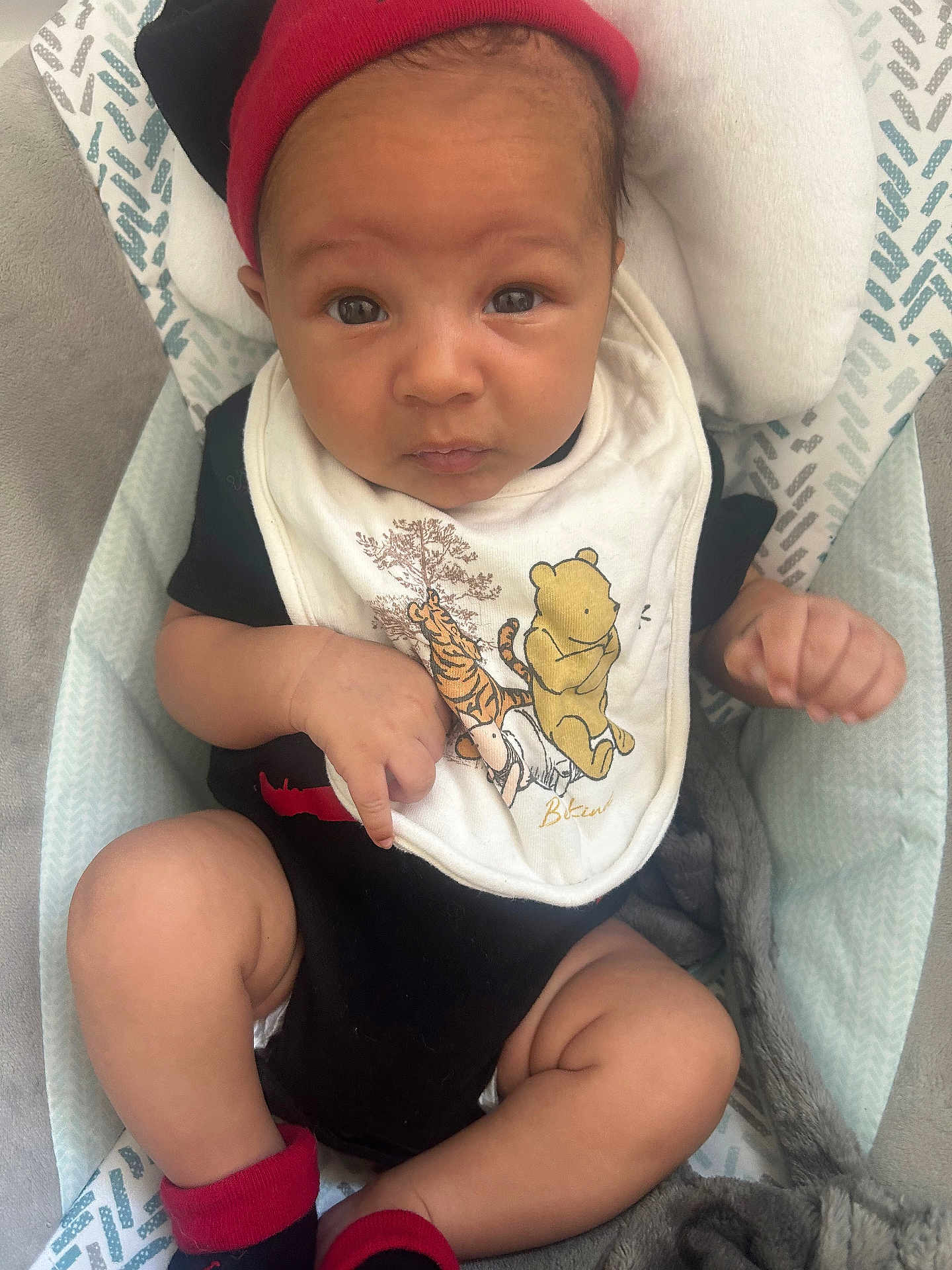 Xayvièn is registered to the contest to win money with this photo: baby, infant, child, face, headwear, bib, winnie_the_pooh, red_hat, black_clothing, socks, blanket, cushion, seated, indoors, cute, expression, looking, soft_texture, comfort, closeup