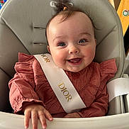Giulia a rejoint le concours — aidez-le/la à gagner de superbes lots ! baby, high_chair, smiling, child, indoor, clothing, sash, pink, happy, person, face, hand, hair, furniture, cute, portrait, dior, infant, seat, young