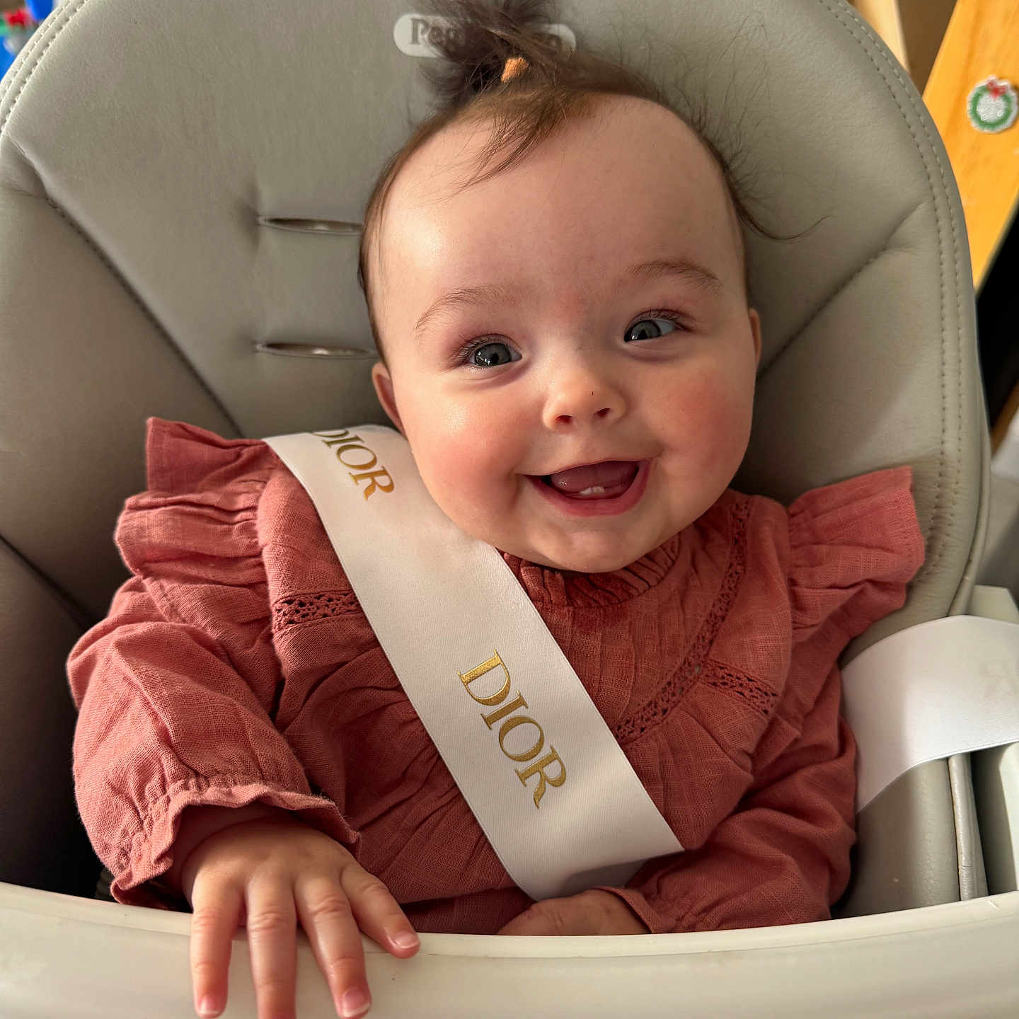 Giulia a rejoint le concours — aidez-le/la à gagner de superbes lots ! baby, high_chair, smiling, child, indoor, clothing, sash, pink, happy, person, face, hand, hair, furniture, cute, portrait, dior, infant, seat, young