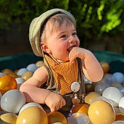 Elio a rejoint le concours — aidez-le/la à gagner de superbes lots ! toddler, child, ball_pit, hat, bib, plastic_balls, outdoor, happy, smiling, sunlight, greenery, play, cute, baby, portrait, cheerful, summer, fun, closeup, colorful