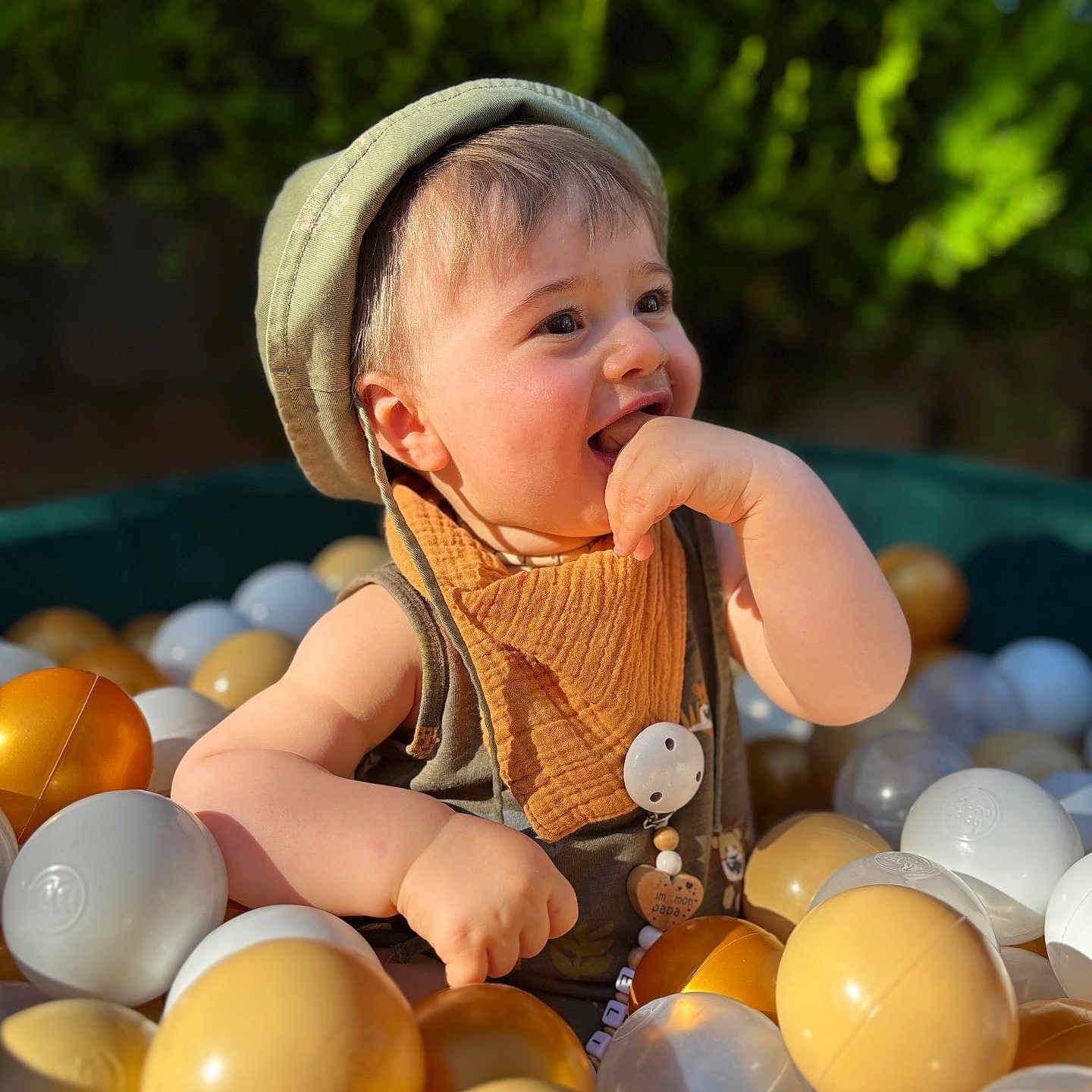 Elio a rejoint le concours — aidez-le/la à gagner de superbes lots ! baby, ball_pit, bib, cheerful, child, closeup, colorful, cute, fun, greenery, happy, hat, outdoor, plastic_balls, play, portrait, smiling, summer, sunlight, toddler