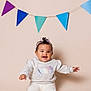 baby, child, smiling, sitting, headband, sweater, barefoot, indoor, colorful_flags, decoration, cute, happy, portrait, infant, studio, soft_lighting, celebration, clothing, young, person