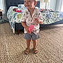 Colton is registered to the contest to win money with this photo: toddler, child, smiling, indoor, bedroom, carpet, toy, shorts, shirt, sandals, bed, pillow, lamp, window, curtains, floor, furniture, happy, person, home