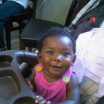 Kamiah Frelix joined the competition — help win amazing prizes! toddler, child, high_chair, smiling, pink_clothing, indoor, furniture, bed, blanket, happy, person, baby, seat, home, portrait, cute, young_child, infant, bright_eyes, hands