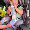 baby, car_seat, bottle, milk, child, infant, seatbelt, car_interior, sunlight, clothing, patterned_pants, smiling, happy, sitting, young_child, cute, portrait, daylight, safety, vehicle