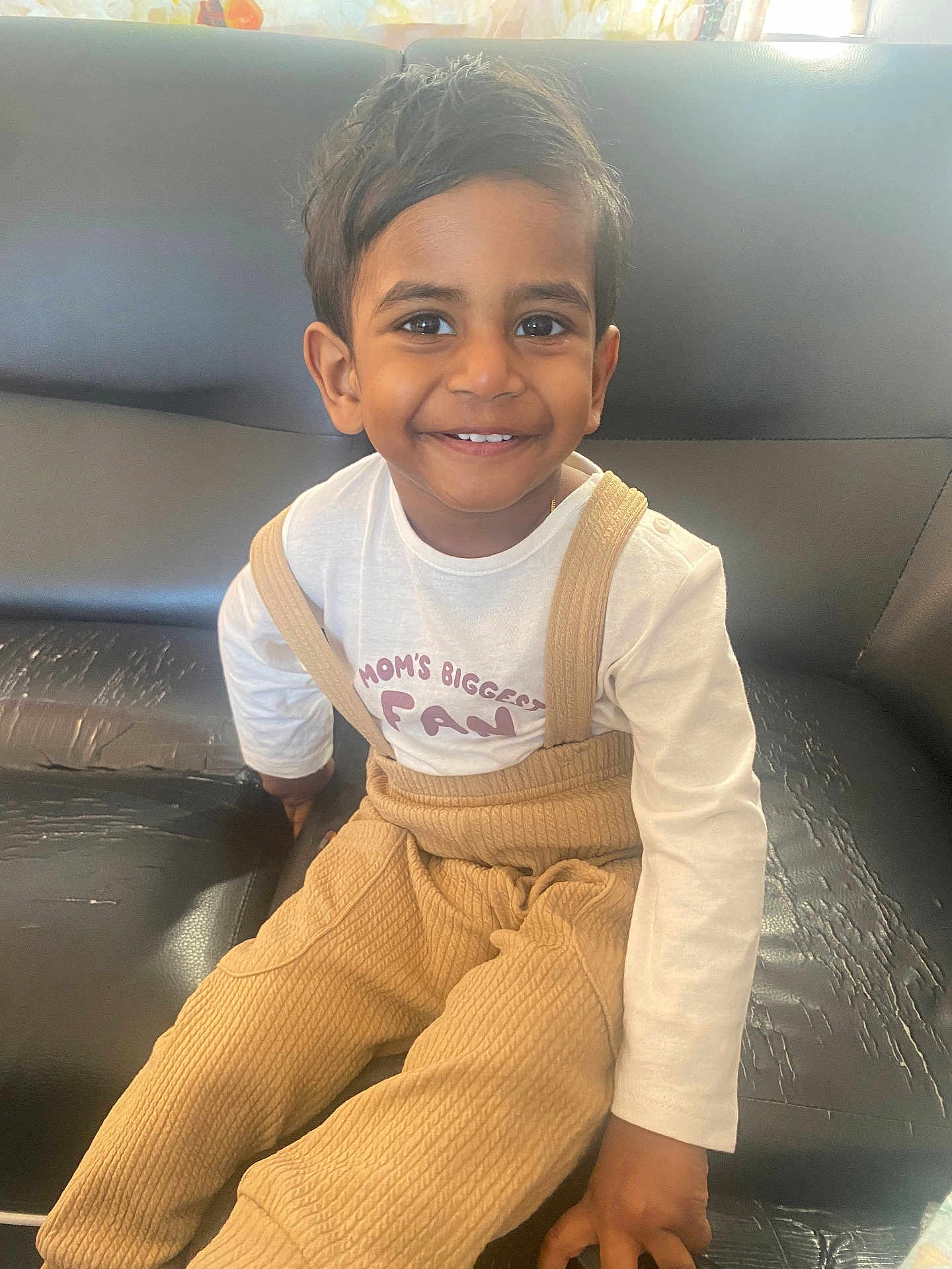 Advihan a rejoint le concours — aidez-le/la à gagner de superbes lots ! child, toddler, smile, happy, portrait, sitting, sofa, couch, tan_overalls, white_shirt, indoors, young_child, face, eyes, hair, hand, casual_clothing, playful, living_room, closeup