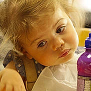 Bonnie is registered to the contest to win money with this photo: toddler, child, face, blonde_hair, curly_hair, high_chair, purple_bottle, portrait, expression, indoor, soft_light, closeup, clothing, bib, young_child, person, baby, cute, skin, head