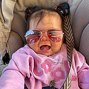 Ahytana a rejoint le concours — aidez-le/la à gagner de superbes lots ! baby, child, sunglasses, pink_sweatshirt, car_seat, seatbelt, smiling, happy, cute, portrait, clothing, accessory, indoors, infant, person, fashion, casual, hair, seat, closeup