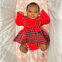 adorable, baby, bassinet, blanket, child, comfortable, cozy, curly_hair, cute, fashion, indoors, infant, lying_down, plaid, portrait, red_dress, small_fists, soft_texture, star_pattern, white_socks
