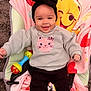 baby, smile, headband, toy, blanket, winnie_the_pooh, child, rattle, sitting, happy, clothing, indoor, cute, infant, black_pants, sweater, face, person, carseat, pink