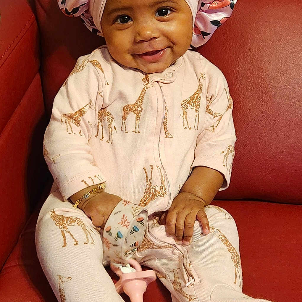 Amira is registered to the contest to win money with this photo: baby, bonnet, cap, clothing, couch, cushion, face, furniture, happy, hat, head, homedecor, hosiery, person, photography, portrait, scarf, sitting, smile, sock