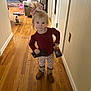 child, toddler, girl, bow, phone, sippy_cup, boots, hardwood_floor, hallway, living_room, toy, ride_on_toy, sofa, fireplace, door, sign, smile, standing, portrait, clothing