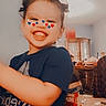 London is registered to the contest to win money with this photo: child, smiling, happy, portrait, indoor, home, face, grin, teeth, heart_stickers, playful, dark_shirt, curly_hair, standing, arm, furniture, cabinet, table, carpet, photography