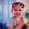toddler, child, smiling, portrait, indoors, digital_filter, sparkles, red_hair_buns, phone, handheld_device, blue_curtain, fan, seated, short_sleeves, t_shirt, happy, face, eyes, home, photography