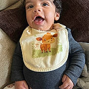 Kashius joined the competition — help win amazing prizes! baby, bib, child, clothing, couch, curly_hair, cute, face, giraffe, hand, happy, indoor, infant, pants, person, pillow, portrait, seated, smiling, teddy_bear_pattern
