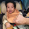 baby, baby_toys, bib, blanket, car_seat, child, clothing, cozy, curly_hair, cute, hand, happy, indoor, infant, pacifier, person, portrait, seatbelt, smiling, toddler