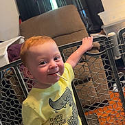 Oliver joined the competition — help win amazing prizes! toddler, child, smiling, yellow_shirt, crocodile_graphic, indoor, living_room, safety_gate, wood_floor, recliner_chair, window, playful, red_hair, shorts, person, cute, happy, chewing, handrail, home
