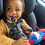 action_figure, black_panther, car_interior, car_seat, child, clothing, curly_hair, face, hands, happy, indoor, playful, plush_toy, portrait, seatbelt, smiling, spiderman, sweater, toddler, toy