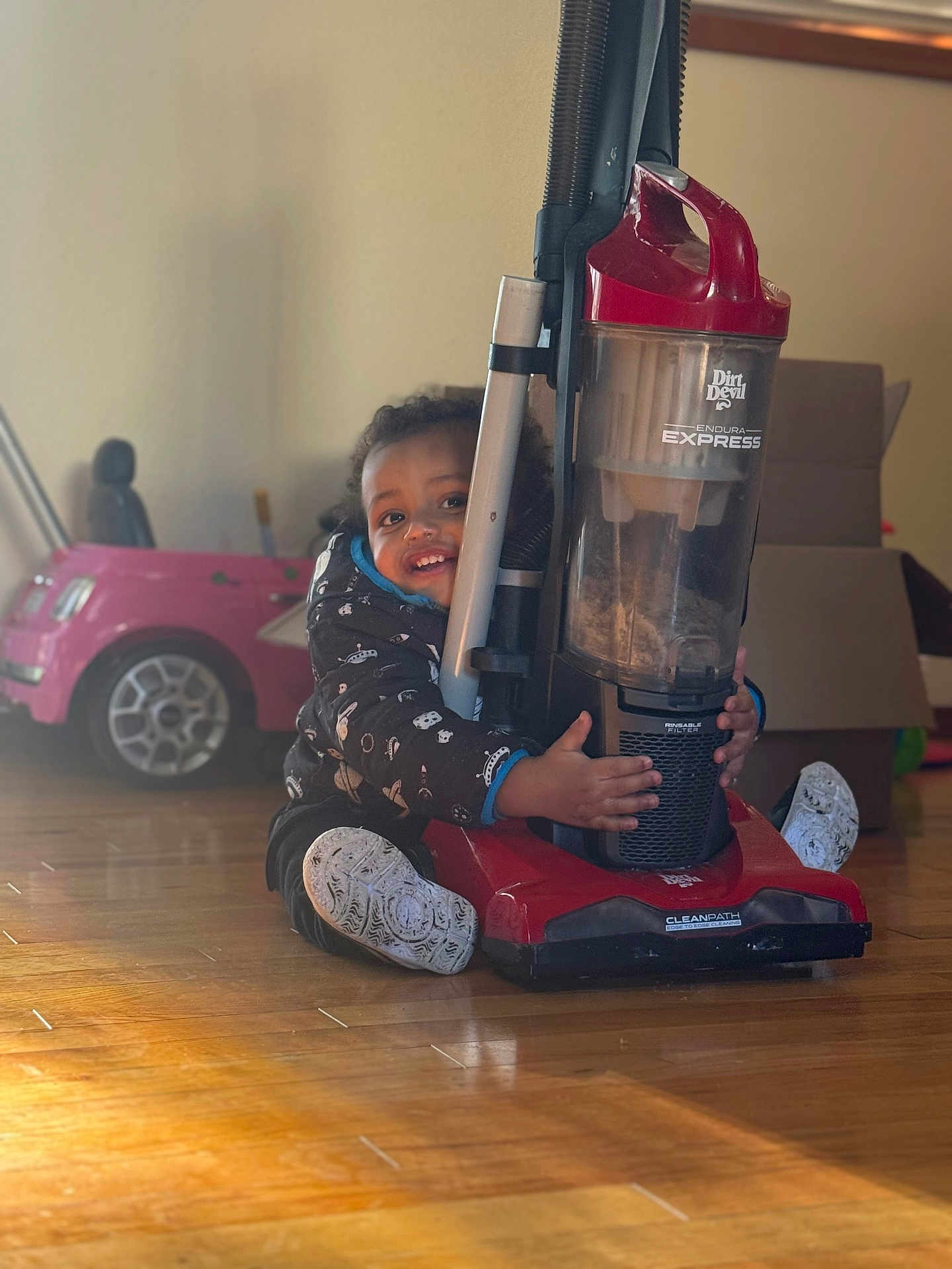 Jahqaari is registered to the contest to win money with this photo: appliance, child, cleaning, clothing, floor, footwear, furniture, happy, home, hug, indoor, light, person, playful, room, smile, toddler, toy_car, vacuum_cleaner, wooden_floor