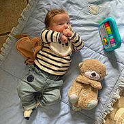 Léon a rejoint le concours — aidez-le/la à gagner de superbes lots ! baby, infant, striped_shirt, denim_pants, pacifier, blue_blanket, plush_toy, teddy_bear, toy_piano, floor, soft_toy, child, cute, indoors, casual_clothing, lying_down, curious, playtime, comfortable, cozy