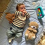 baby, infant, striped_shirt, denim_pants, pacifier, blue_blanket, plush_toy, teddy_bear, toy_piano, floor, soft_toy, child, cute, indoors, casual_clothing, lying_down, curious, playtime, comfortable, cozy