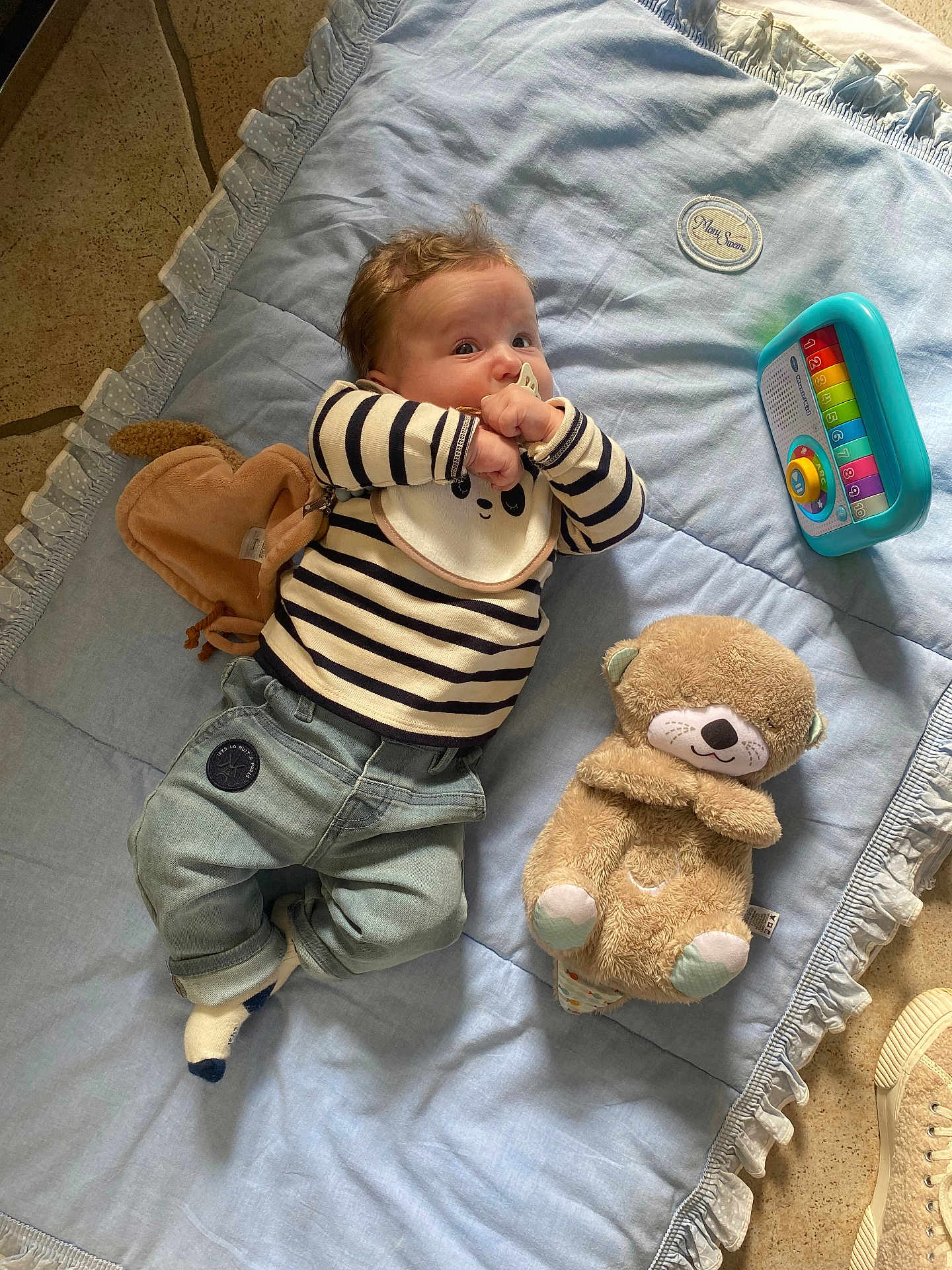 Léon a rejoint le concours — aidez-le/la à gagner de superbes lots ! baby, infant, striped_shirt, denim_pants, pacifier, blue_blanket, plush_toy, teddy_bear, toy_piano, floor, soft_toy, child, cute, indoors, casual_clothing, lying_down, curious, playtime, comfortable, cozy