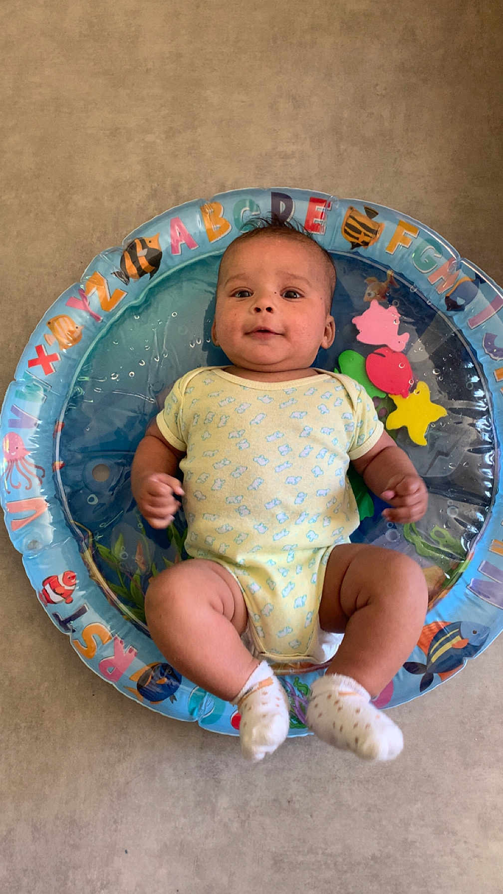 Maël a rejoint le concours — aidez-le/la à gagner de superbes lots ! baby, infant, onesie, socks, inflatable_ring, alphabet, sea_creatures, floor, child, smiling, cute, indoor, playtime, floating, water_toy, colorful, young_child, happy, portrait, person