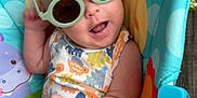 August is registered to the contest to win money with this photo: baby, sunglasses, child, colorful, animal_print, seat, playful, smiling, summer, cute, infant, clothing, green_shorts, tank_top, indoor, joyful, fun, accessory, portrait, happy