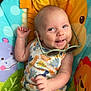 baby, infant, smiling, sunglasses, dinosaur_print, colorful, seat, animal_theme, playful, child, cute, happy, clothing, green_shorts, indoor, portrait, toy, hand, face, expression