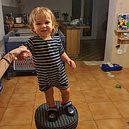 Arthur a rejoint le concours — aidez-le/la à gagner de superbes lots ! toddler, child, striped_pajamas, slippers, stool, hand_holding, indoor, kitchen, tile_floor, toy_car, furniture, person, smile, curly_hair, home, warm_lighting, adult_hand, background, cabinet, plant