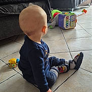 Léo participe au concours pour gagner de l'argent avec cette photo : baby, child, indoor, floor, tile, socks, toy, sofa, blanket, couch, living_room, clothing, person, toddler, home, furniture, window, daylight, playtime, casual