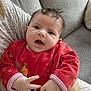Olivia a rejoint le concours — aidez-le/la à gagner de superbes lots ! baby, infant, red_onesie, hand, face, expression, couch, adult_arm, curly_hair, indoor, person, skin, furniture, cozy, child, cute, sitting, clothing, portrait, happy