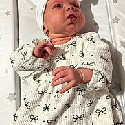 Olivia is registered to the contest to win money with this photo: baby, infant, child, white_clothing, head_wrap, patterned_dress, hand, face, expression, shadow, star_pattern, padded_surface, cute, indoors, portrait, newborn, soft_light, skin, laying_down, curious