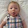 baby, child, tongue_out, plaid, colorful_clothing, infant, cute, text_overlay, question, white_background, face, portrait, young_child, expression, lying_down, buttoned_overalls, short_sleeves, human, skin, funny