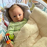 Maximillian is registered to the contest to win money with this photo: baby, infant, blanket, toy, caterpillar_toy, green_clothing, hood, ears, face, hand, indoor, soft_texture, bedroom, comfort, cute, child, person, expression, warm_light, relaxed