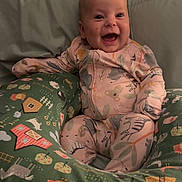 Charlee is registered to the contest to win money with this photo: baby, child, smiling, onesie, pillow, cushion, animal_print, farm_theme, indoor, happy, person, infant, cute, comfortable, seated, face, head, expression, clothing, soft