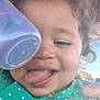 toddler, child, curly_hair, tongue_out, green_shirt, polka_dots, cup, hand, outdoor, sky, playful, close_up, smile, buttoned_shirt, face, person, happy, daylight, expression, young_child