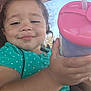 Xariah is registered to the contest to win money with this photo: toddler, child, curly_hair, smile, green_shirt, polka_dot, sippy_cup, hand, face, outdoor, sunny, window, glass, portrait, happy, young_child, skin, person, close_up, daylight