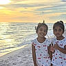 beach, cherry_pattern, children, dresses, family, girls, matching_outfits, ocean, outdoor, portrait, sand, seaside, shoreline, siblings, smiling, sunlight, sunset, thumbs_up, vacation, waves