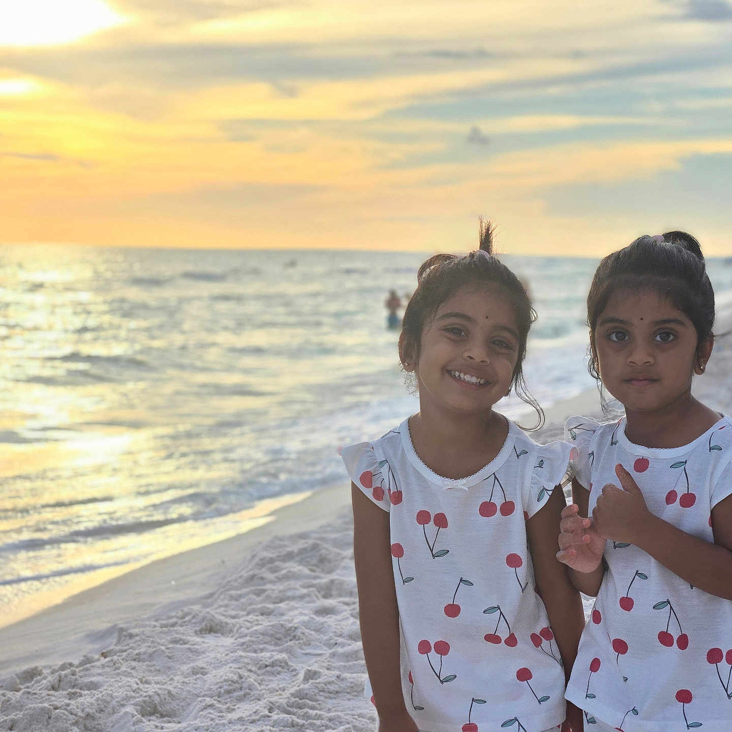 Aarvi Patel is registered to the contest to win money with this photo: beach, cherry_pattern, children, dresses, family, girls, matching_outfits, ocean, outdoor, portrait, sand, seaside, shoreline, siblings, smiling, sunlight, sunset, thumbs_up, vacation, waves