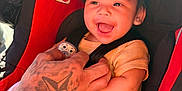 Josiah joined the competition — help win amazing prizes! baby, child, car_seat, smiling, tattoo, hand, pacifier, blanket, clothing, infant, seatbelt, red, black, yellow, cute, happy, portrait, closeup, person, sitting
