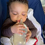 Armani joined the competition — help win amazing prizes! baby, infant, bottle, milk, blanket, curly_hair, pacifier, red_clip, blue_seat, sleepy, closed_eyes, cute, child, hand, clothing, indoors, cozy, feeding, resting, young