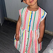 Krystal joined the competition — help win amazing prizes! child, barefoot, striped_dress, curly_hair, wooden_floor, radiator, toy, indoor, playful_expression, person, smiling, standing, home, cute, colorful_clothing, buttoned_dress, young_girl, barefoot_child, portrait