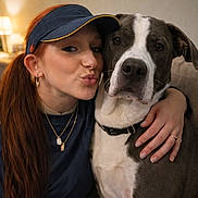 Oakley joined the competition — help win amazing prizes! woman, dog, pet, indoor, portrait, affection, hug, casual_clothing, visor, necklace, brown_hair, white_and_grey_dog, couch, closeup, face, expression, friendship, touch, warm_lighting, cozy