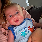 Maëlo participe au concours pour gagner de l'argent avec cette photo : baby, child, person, indoor, couch, smile, blue_clothing, sleeveless_shirt, sea_creatures, hand, adult, curly_hair, window, natural_light, happy, closeup, face, skin, infant, holding