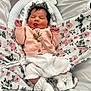 baby, sleeping, tongue_out, pink_cardigan, white_socks, lace, floral_blanket, baby_nest, infant, cute, newborn, cozy, soft, indoors, child, peaceful, resting, clothing, portrait, adorable