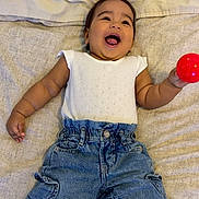 Aliana joined the competition — help win amazing prizes! baby, child, infant, smiling, happy, denim_pants, white_top, red_ball, lying_down, bed, blanket, cute, joyful, playful, portrait, person, indoors, casual_clothing, small_child, cheerful