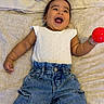 baby, child, infant, smiling, happy, denim_pants, white_top, red_ball, lying_down, bed, blanket, cute, joyful, playful, portrait, person, indoors, casual_clothing, small_child, cheerful