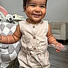 Aliana is registered to the contest to win money with this photo: toddler, child, smile, happy, romper, bow, headwear, indoor, floor, furniture, blanket, plastic, hand, skin, shorts, button, belt, earrings, person, portrait